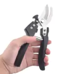 Hand holding a stainless steel bonsai trimmer with black textured handles, open curved blades, against a plain white background