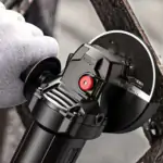 Close-up of a gloved hand operating a black brushless angle grinder against dark metal, with a red spindle lock button visible.