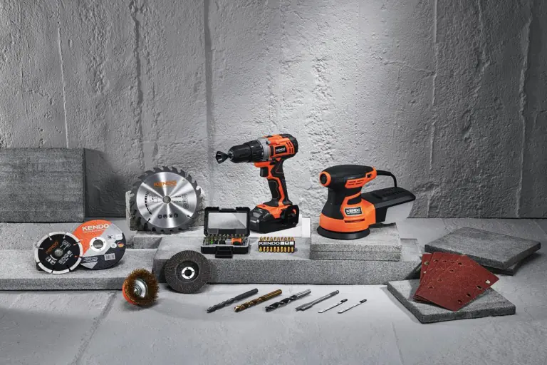 Orange and black cordless drill, orbital sander, saw blades, drill bits, and sanding accessories arranged on gray concrete surfaces