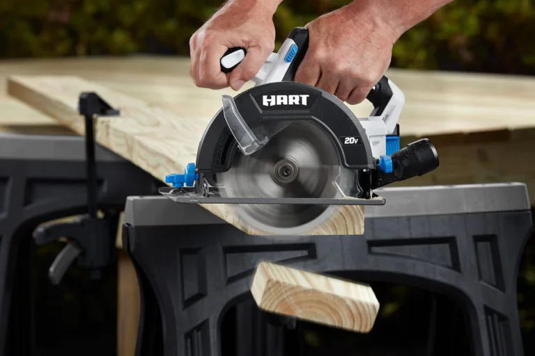 Hands operating a HART 20V cordless circular saw to cut a light wood plank clamped to a black workbench outdoors